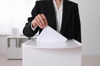 Photo of Woman putting her vote into ballot box indoors, closeup