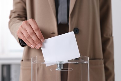 Photo of Woman putting her vote into ballot box indoors, closeup