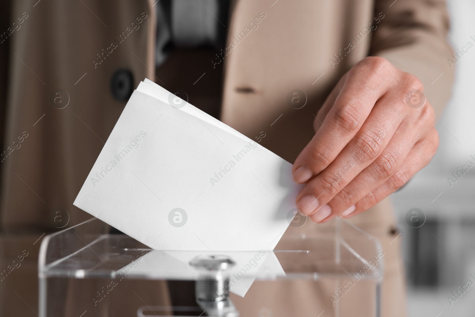 Photo of Woman putting her vote into ballot box indoors, closeup