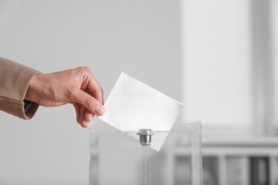 Woman putting her vote into ballot box indoors, closeup