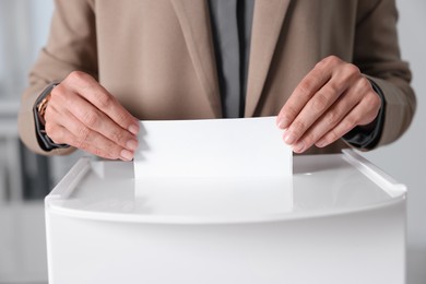 Photo of Woman putting her vote into ballot box indoors, closeup