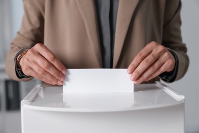 Photo of Woman putting her vote into ballot box indoors, closeup