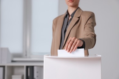 Woman putting her vote into ballot box indoors, selective focus