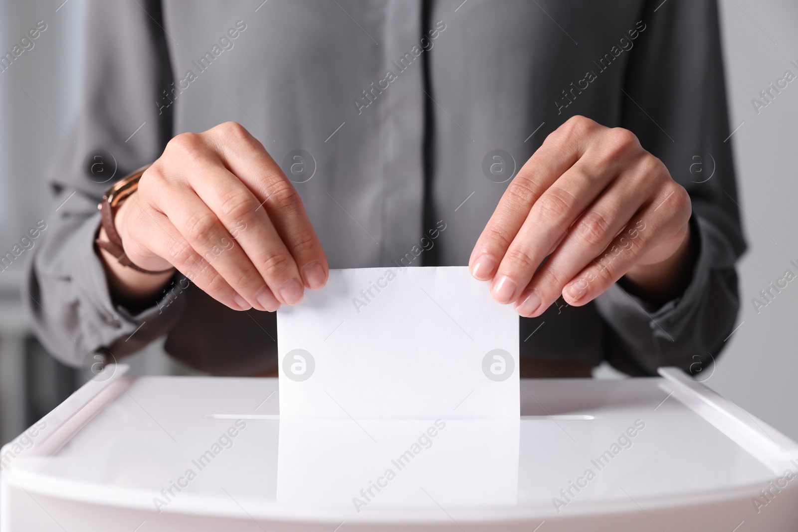 Photo of Woman putting her vote into ballot box indoors, closeup