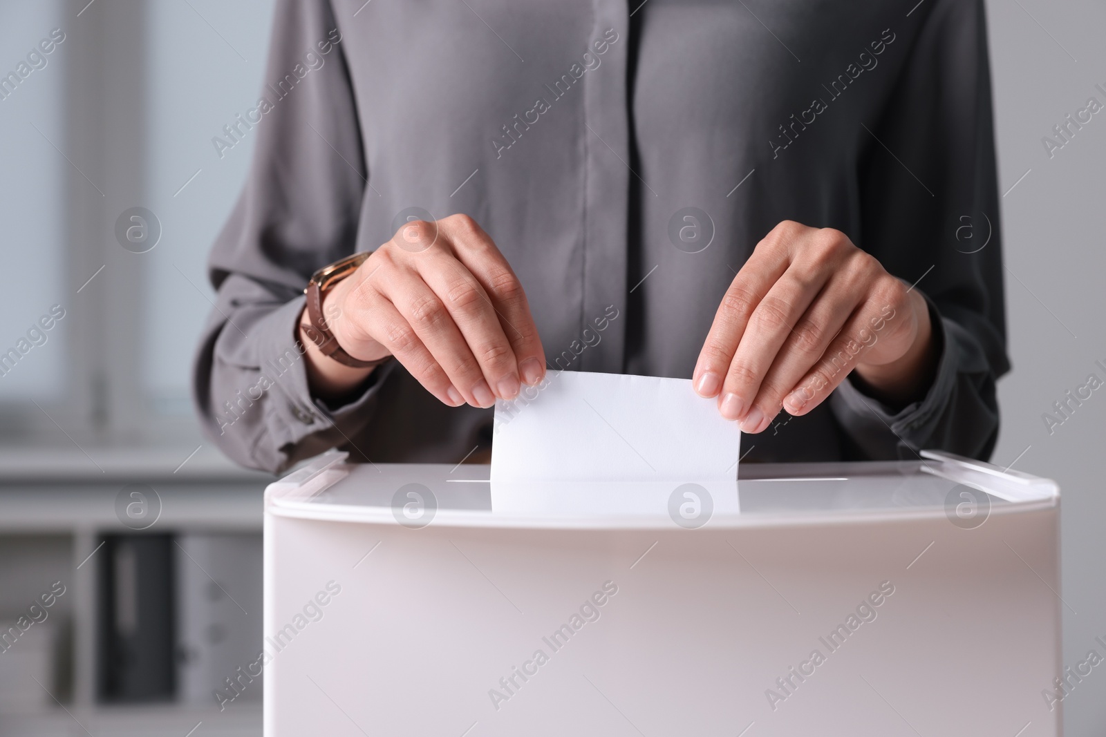 Photo of Woman putting her vote into ballot box indoors, closeup