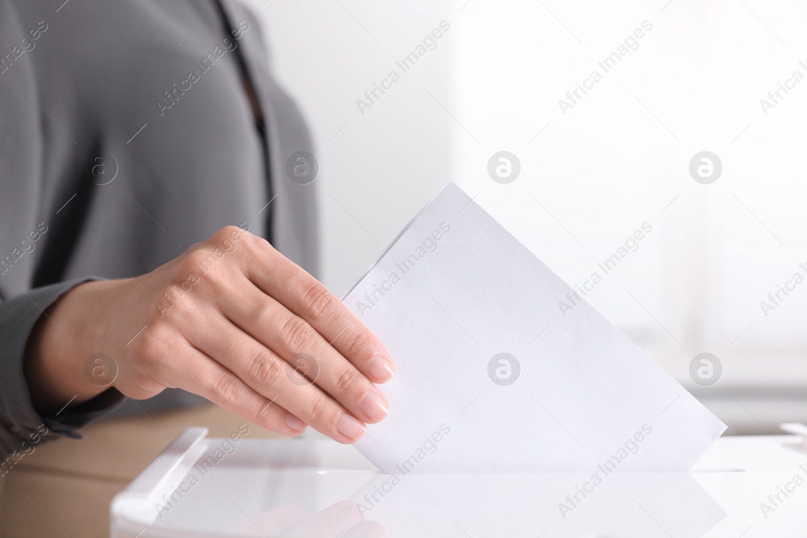 Photo of Woman putting her vote into ballot box indoors, closeup