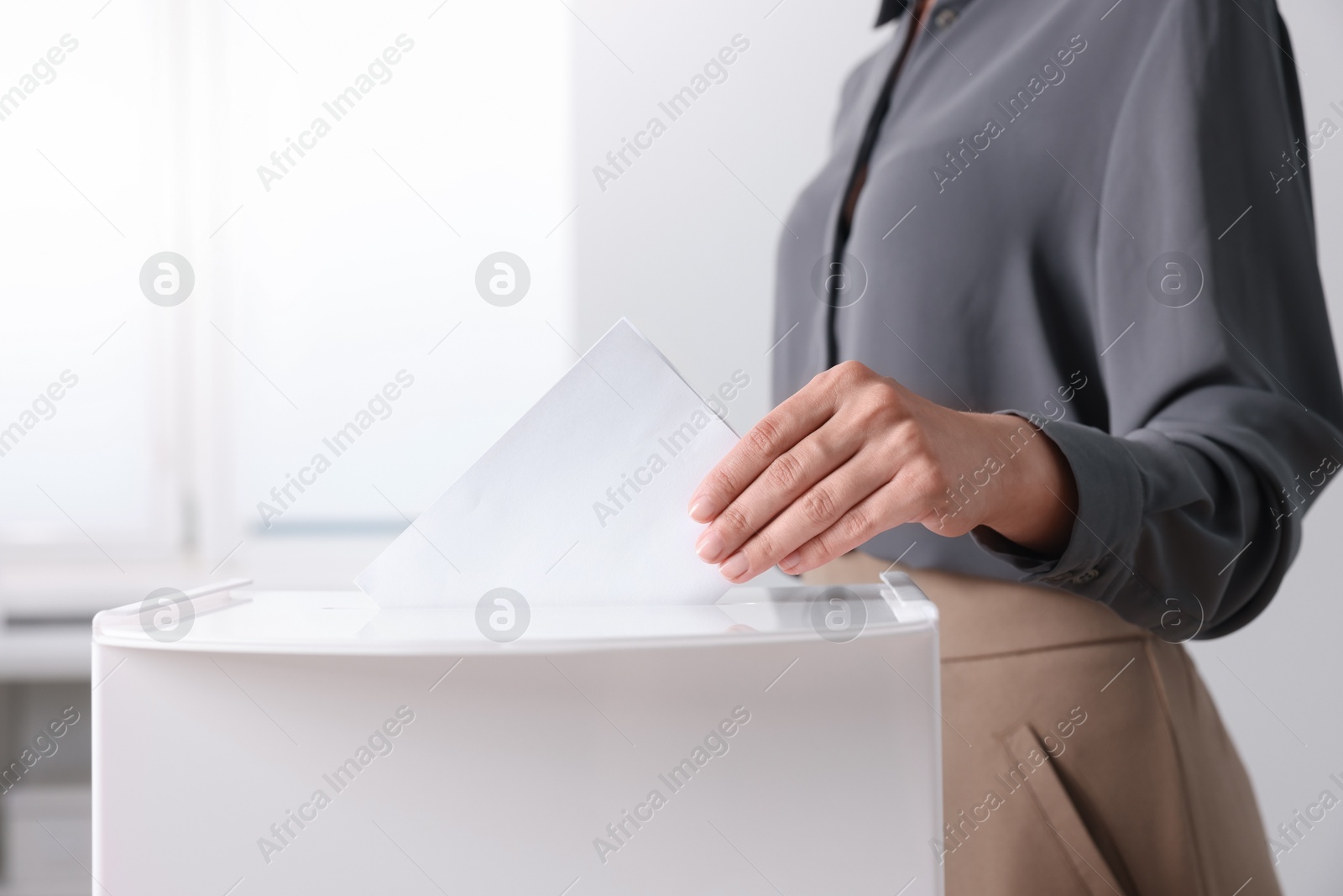 Photo of Woman putting her vote into ballot box indoors, closeup