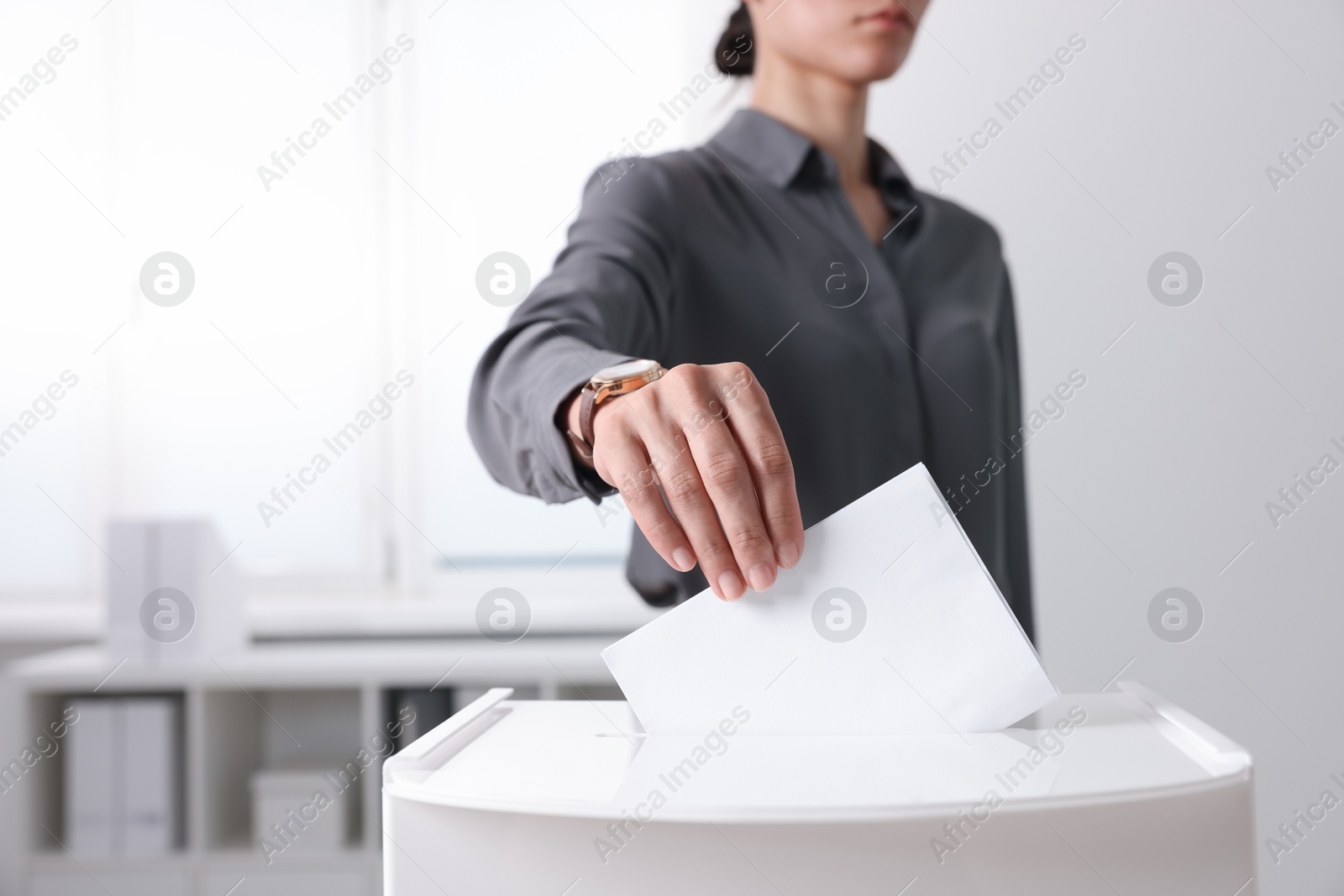 Photo of Woman putting her vote into ballot box indoors, closeup