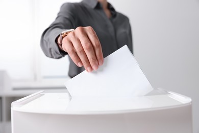 Photo of Woman putting her vote into ballot box indoors, closeup