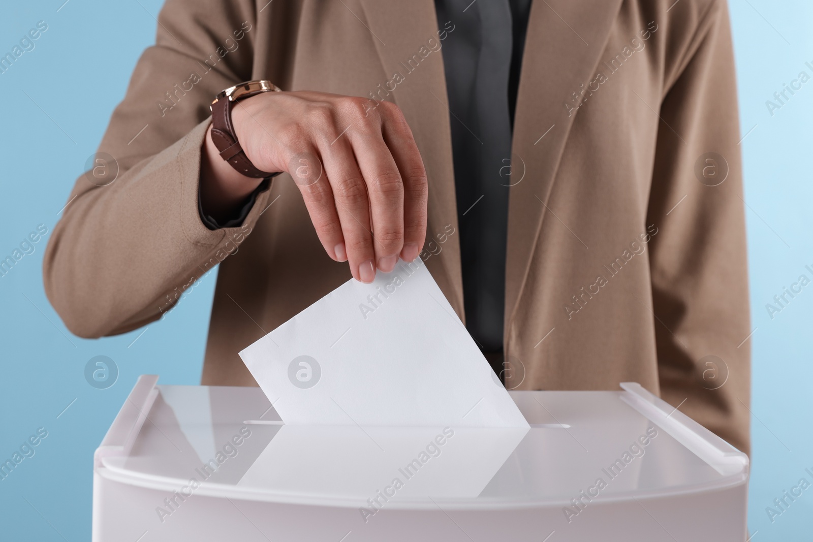 Photo of Woman putting her vote into ballot box against light blue background, closeup