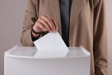 Photo of Woman putting her vote into ballot box against grey background, closeup