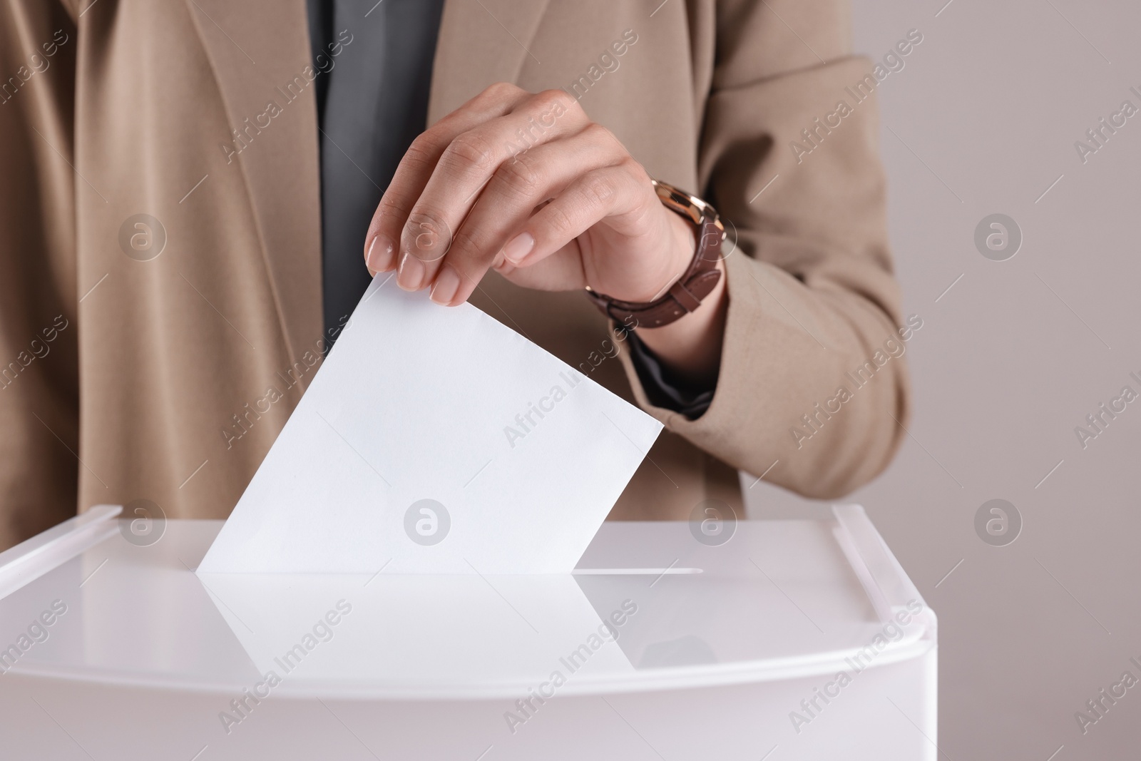 Photo of Woman putting her vote into ballot box against grey background, closeup