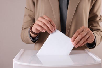 Photo of Woman putting her vote into ballot box against grey background, closeup