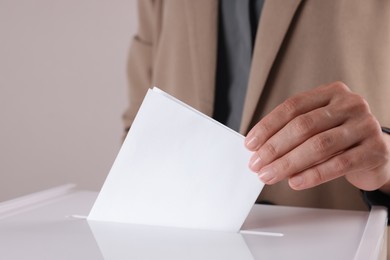 Photo of Woman putting her vote into ballot box against grey background, closeup