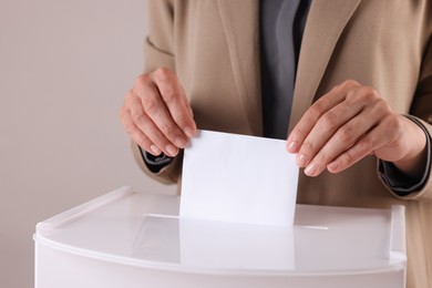 Photo of Woman putting her vote into ballot box against grey background, closeup