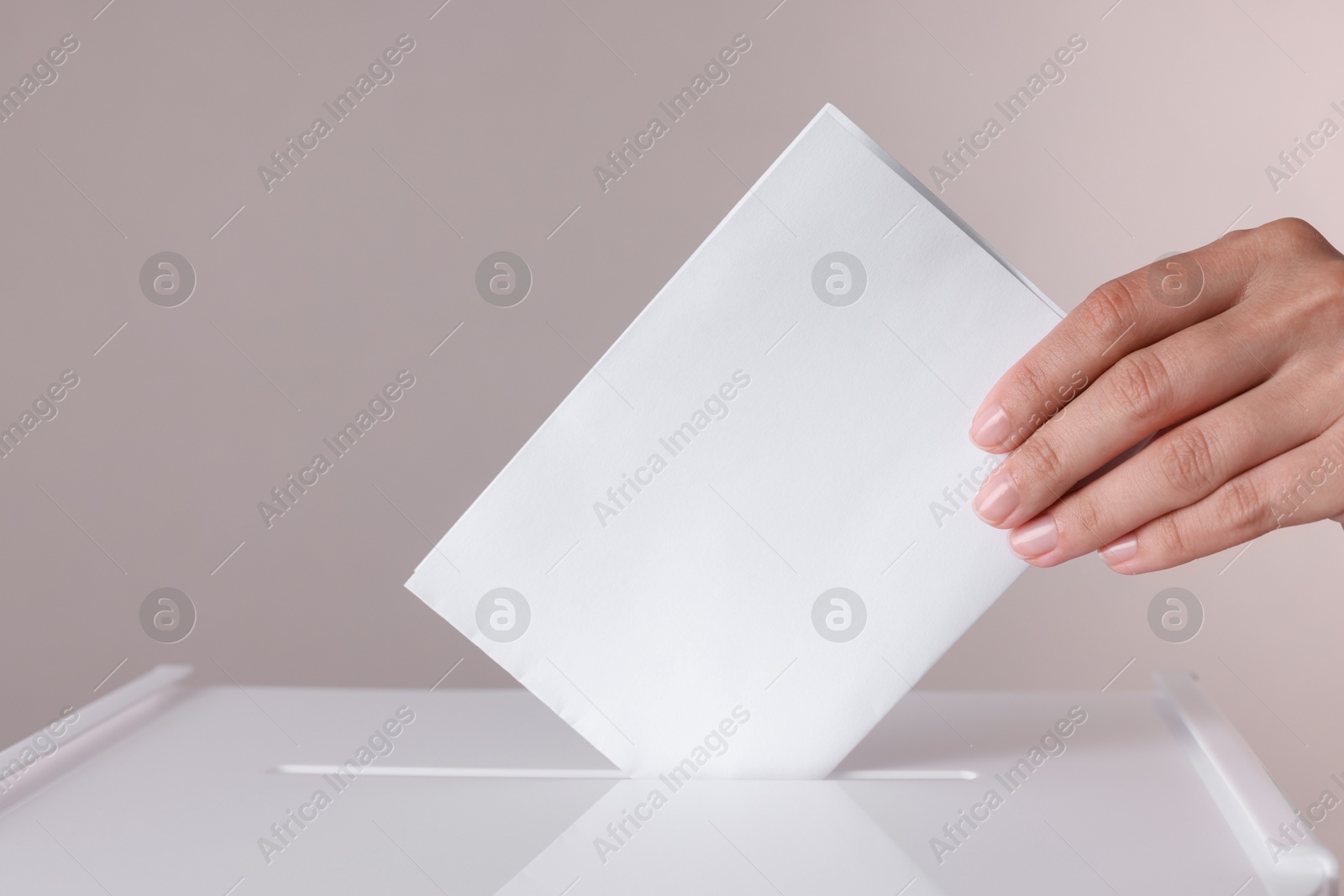 Photo of Woman putting her vote into ballot box against grey background, closeup