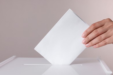 Photo of Woman putting her vote into ballot box against grey background, closeup