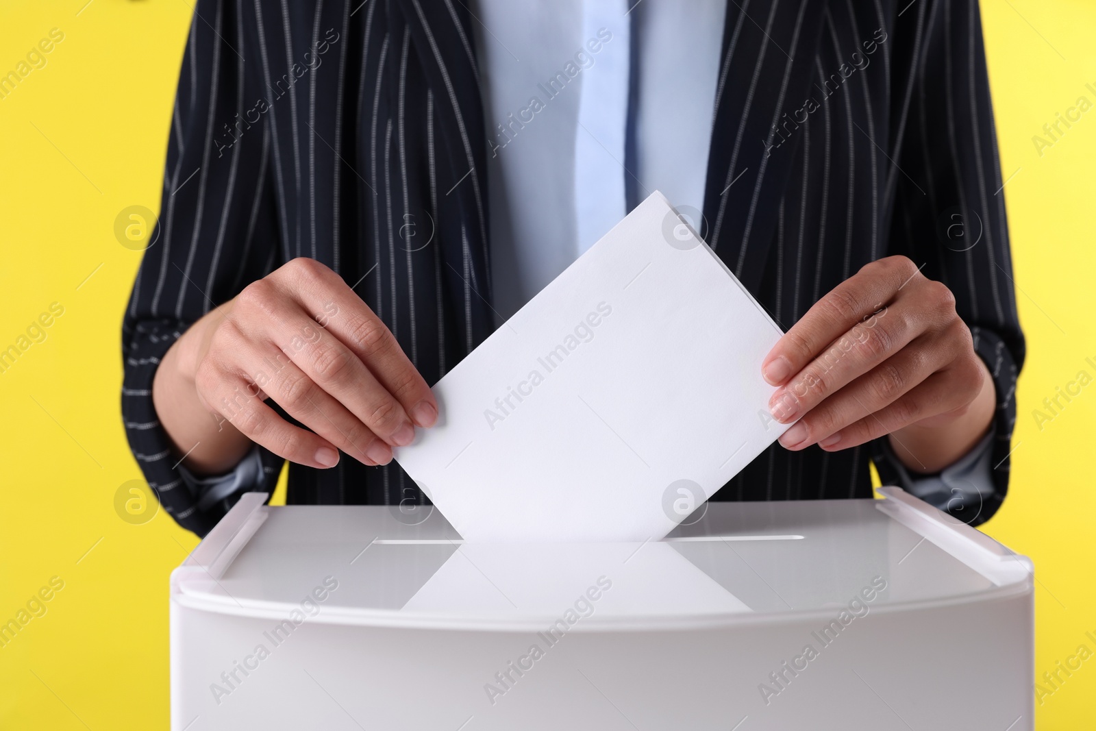 Photo of Woman putting her vote into ballot box against yellow background, closeup