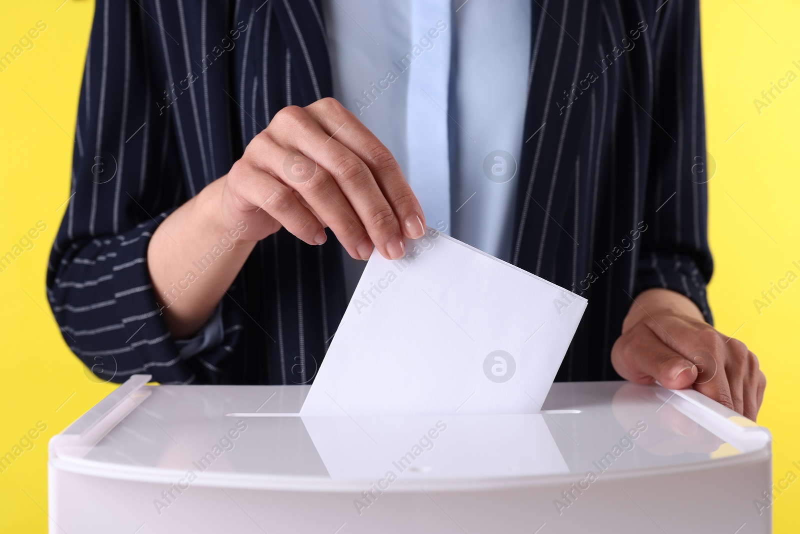 Photo of Woman putting her vote into ballot box against yellow background, closeup