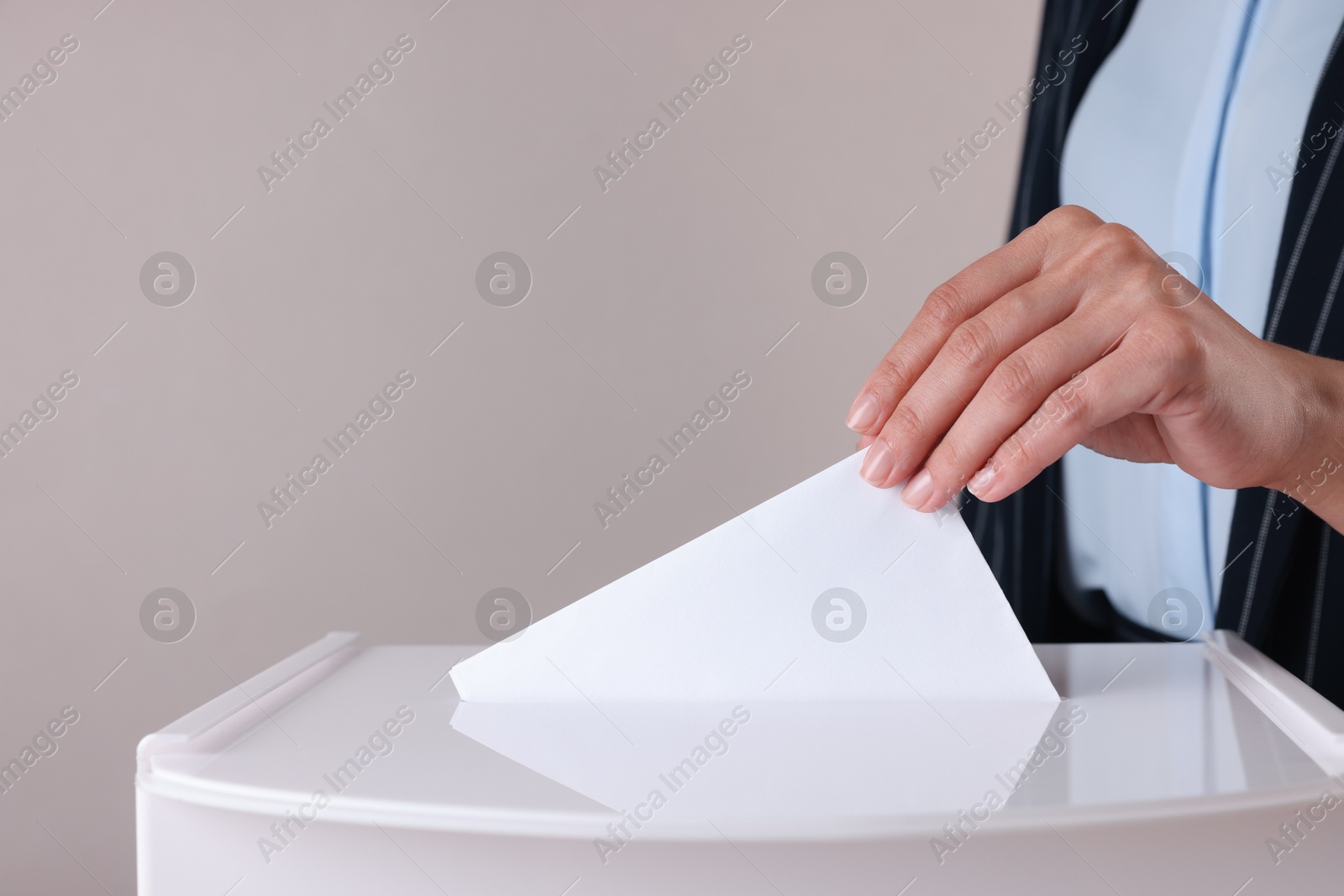 Photo of Woman putting her vote into ballot box against grey background, closeup