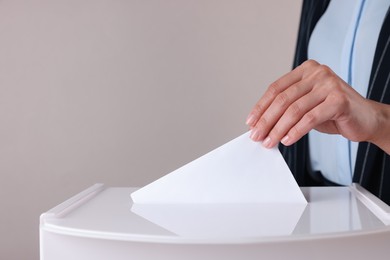 Photo of Woman putting her vote into ballot box against grey background, closeup