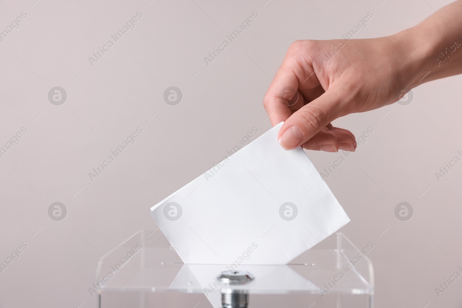 Photo of Woman putting her vote into ballot box against grey background, closeup