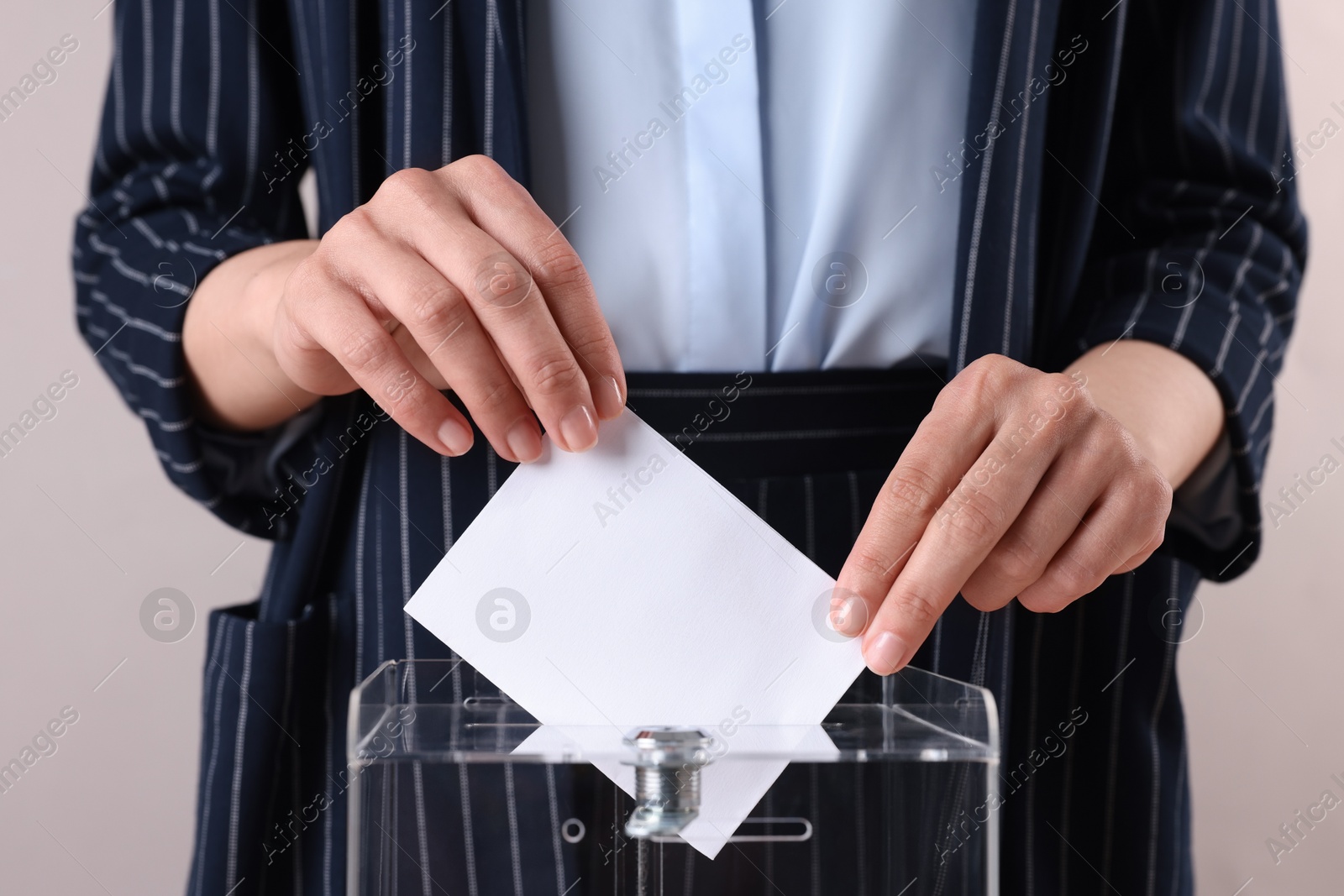 Photo of Woman putting her vote into ballot box against grey background, closeup