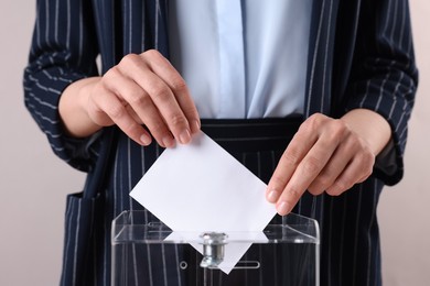 Photo of Woman putting her vote into ballot box against grey background, closeup