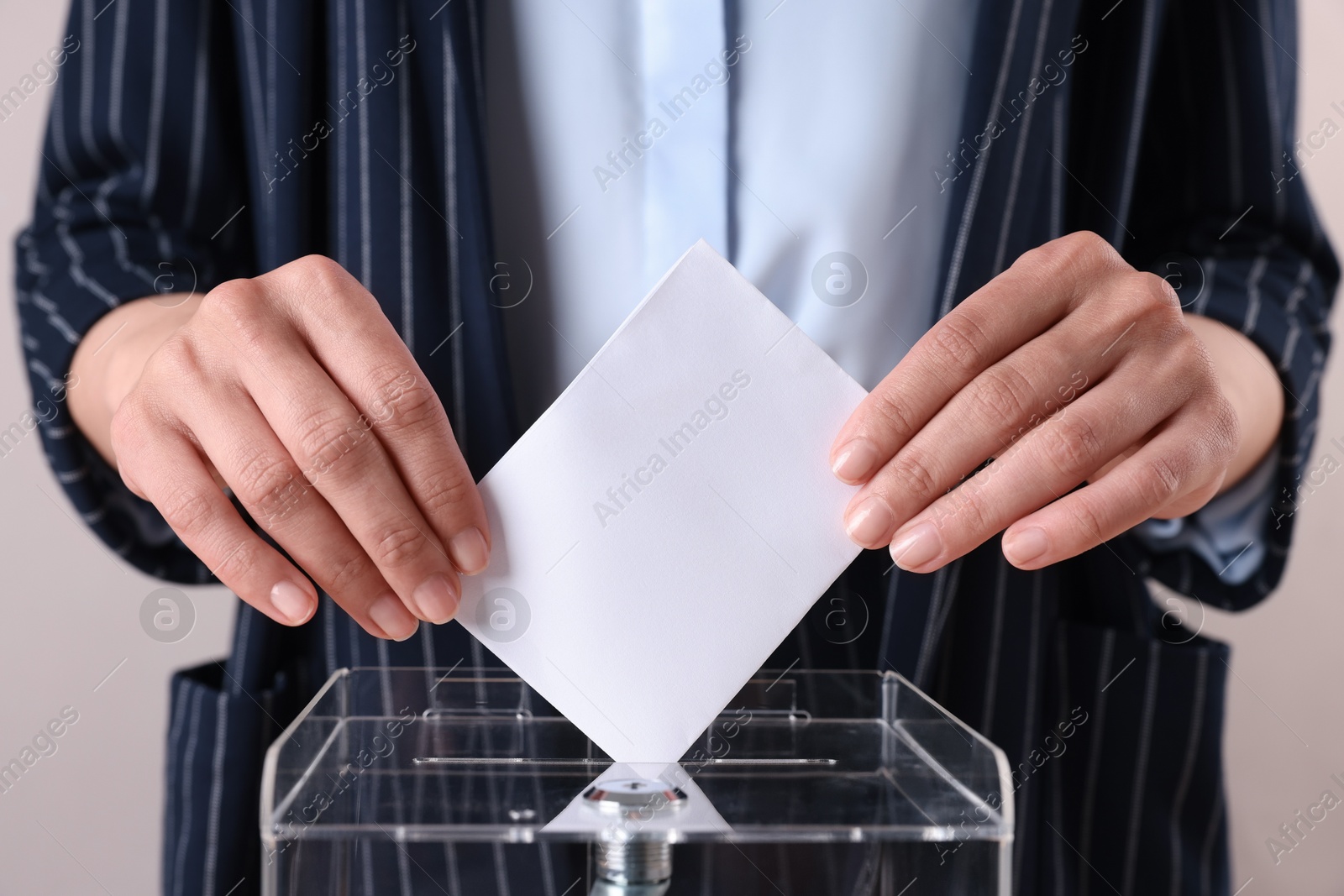 Photo of Woman putting her vote into ballot box against grey background, closeup