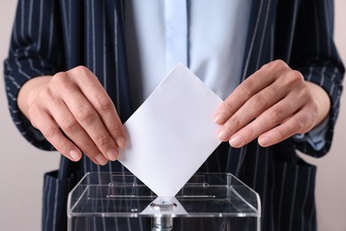 Photo of Woman putting her vote into ballot box against grey background, closeup