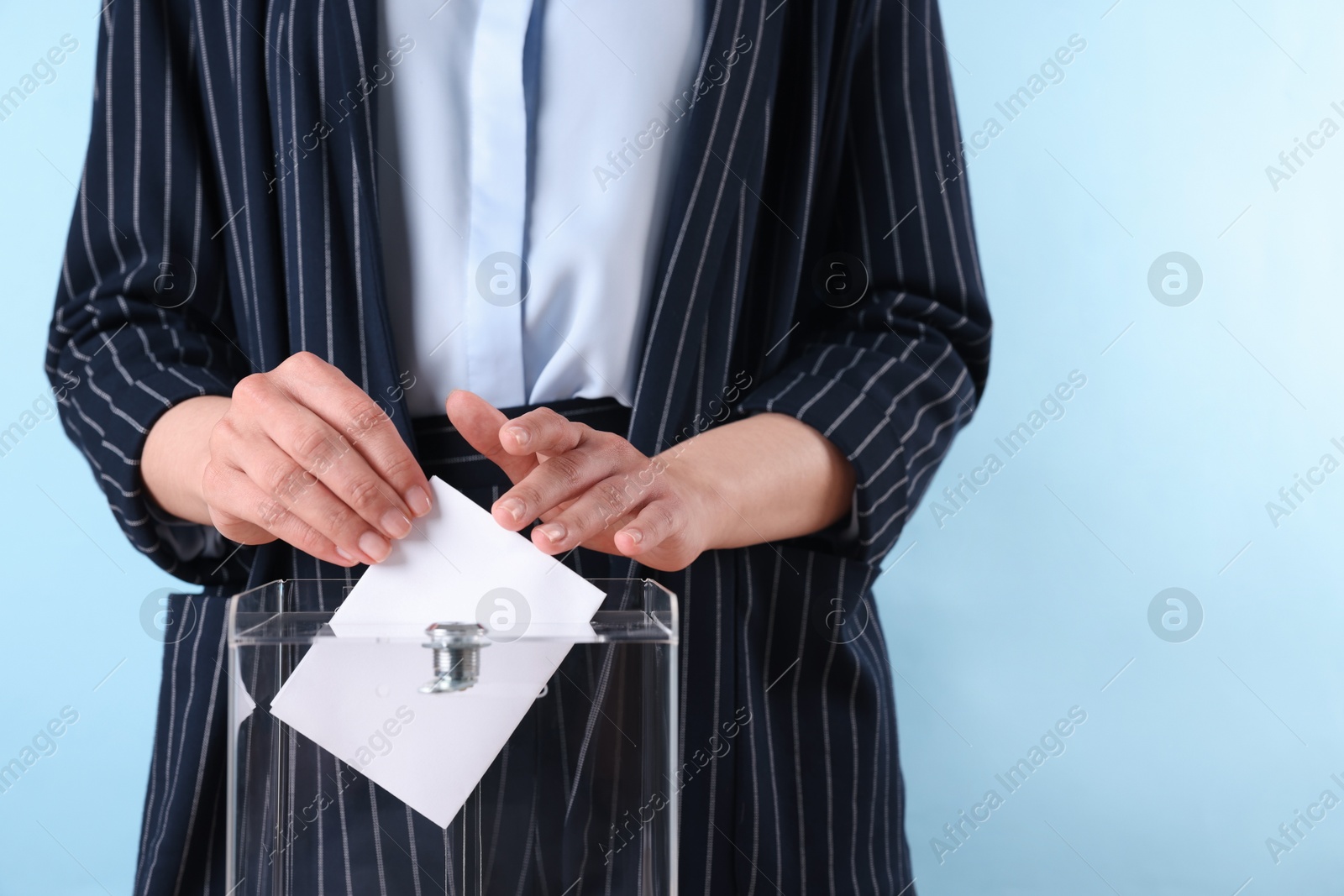 Photo of Woman putting her vote into ballot box against light blue background, closeup