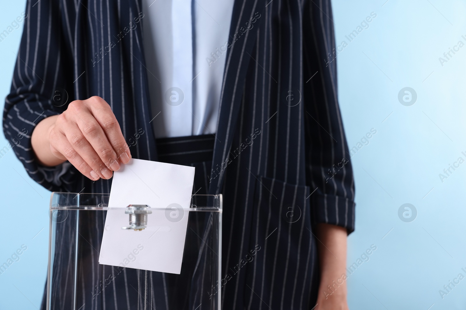 Photo of Woman putting her vote into ballot box against light blue background, closeup