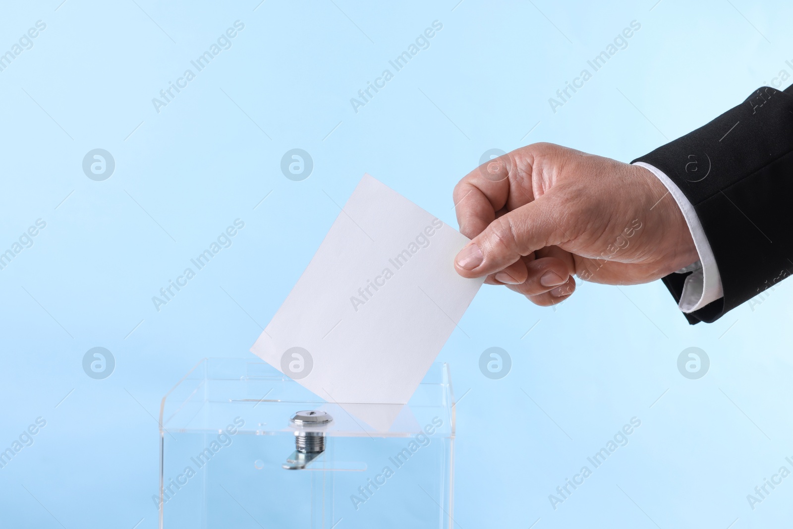 Photo of Man putting his vote into ballot box against light blue background, closeup