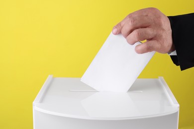 Photo of Man putting his vote into ballot box against yellow background, closeup