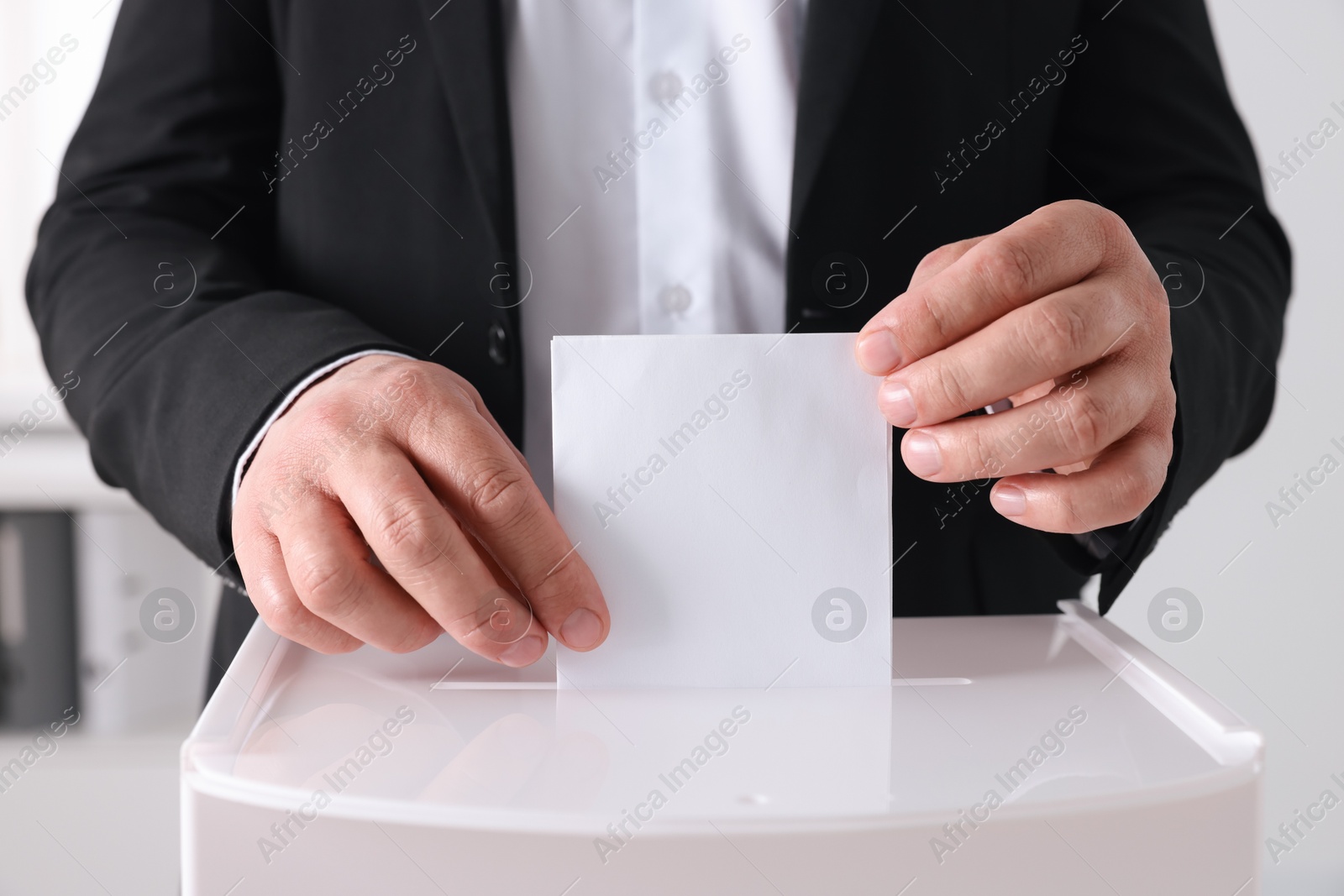 Photo of Man putting his vote into ballot box indoors, closeup