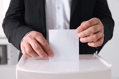 Photo of Man putting his vote into ballot box indoors, closeup