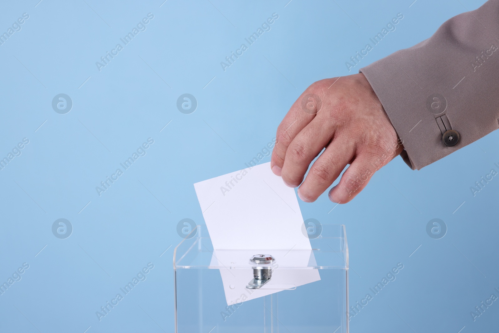 Photo of Man putting his vote into ballot box against light blue background, closeup