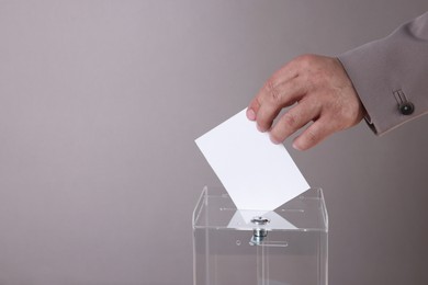 Photo of Man putting his vote into ballot box against grey background, closeup. Space for text