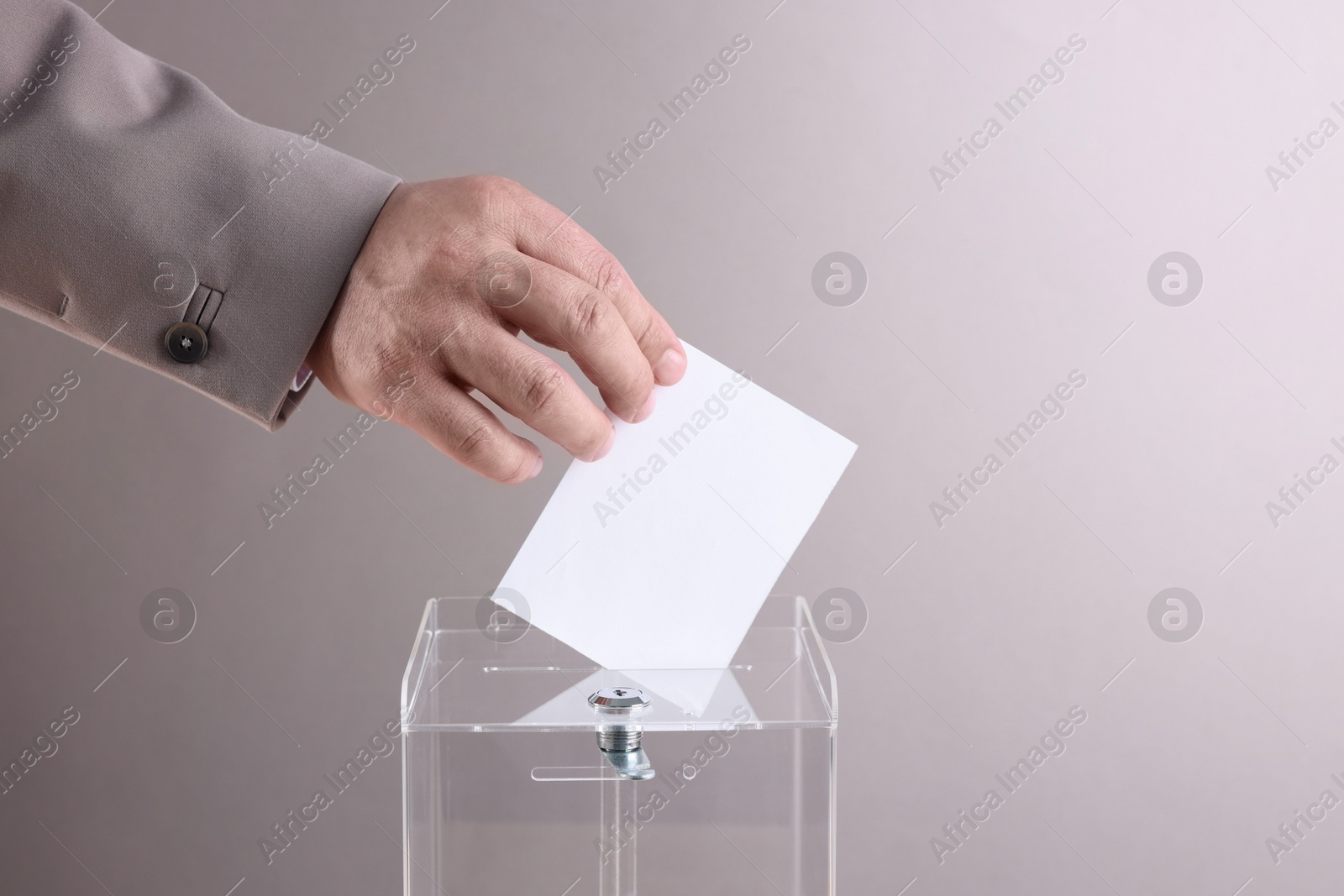 Photo of Man putting his vote into ballot box against light grey background, closeup