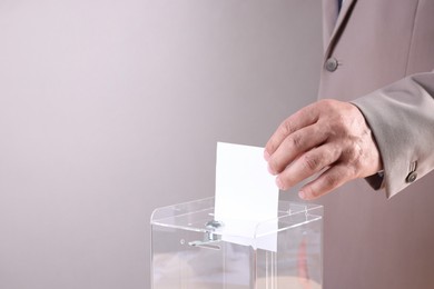 Man putting his vote into ballot box against light grey background, closeup. Space for text