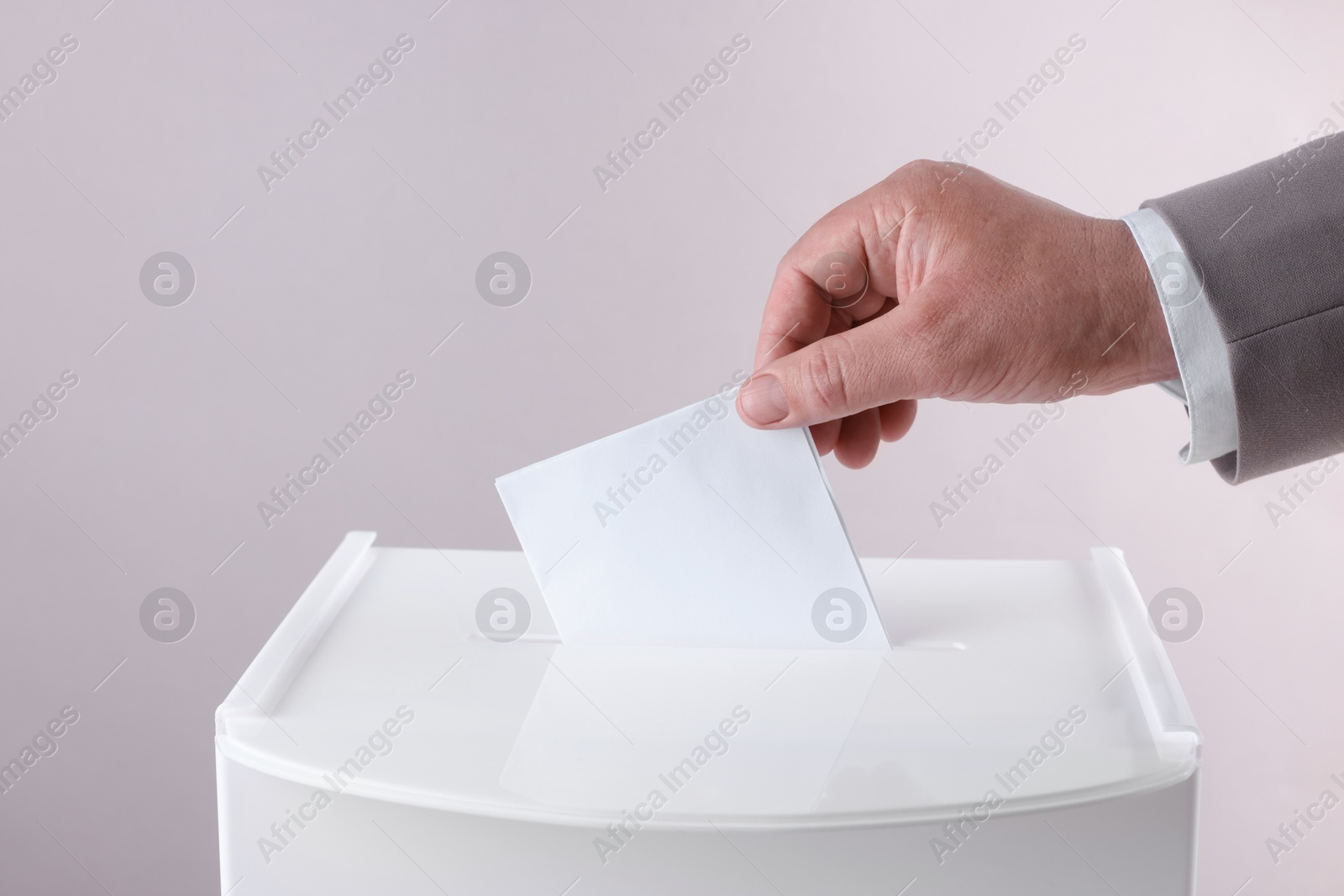 Photo of Man putting his vote into ballot box against light grey background, closeup