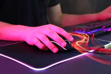 Gamer using modern wired computer mouse in neon lights at dark table, closeup