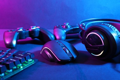 Photo of Computer mouse, headset, RGB keyboard and game controllers in neon lights on dark background, closeup