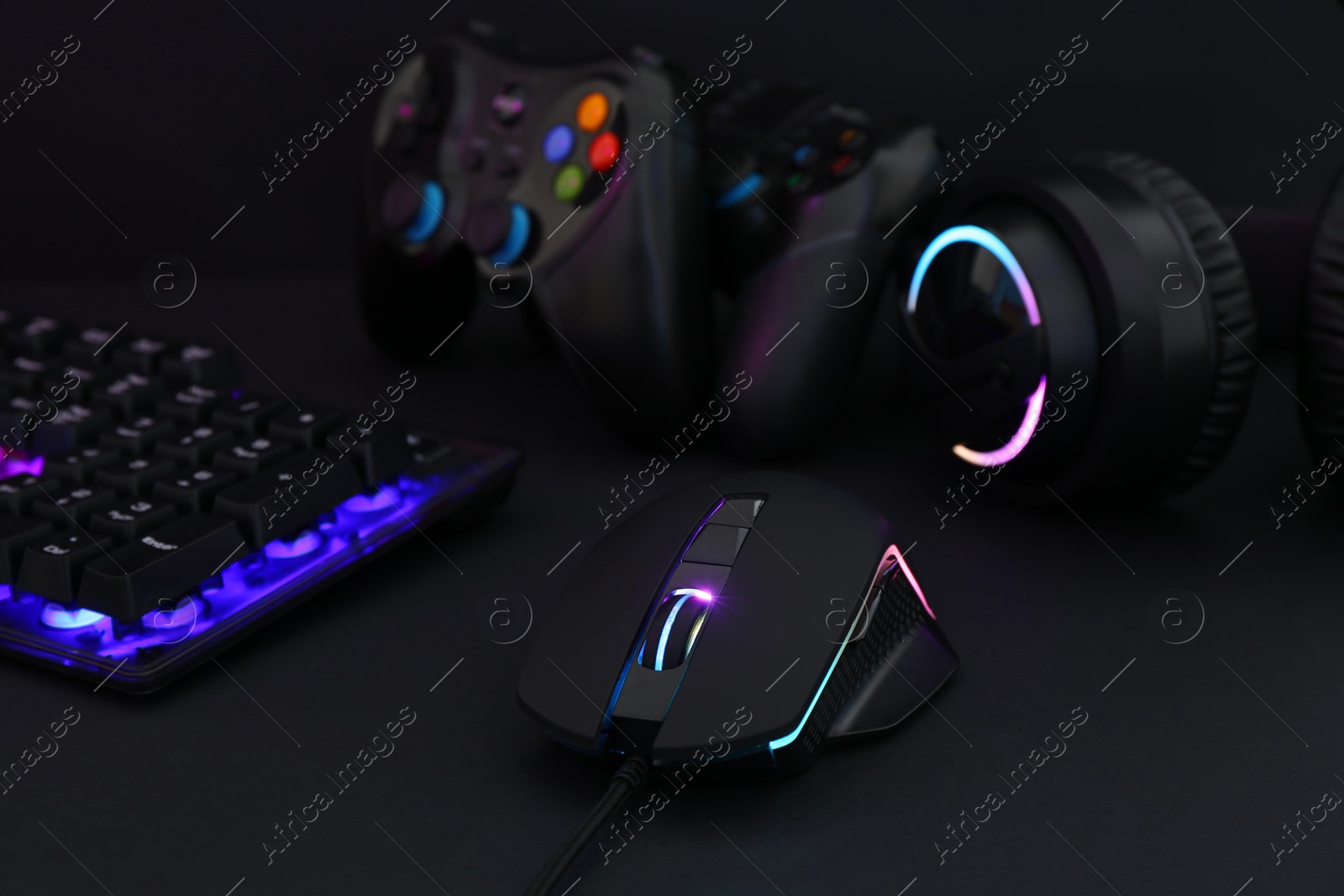 Photo of Computer mouse, headset, RGB keyboard and game controllers on black background, closeup