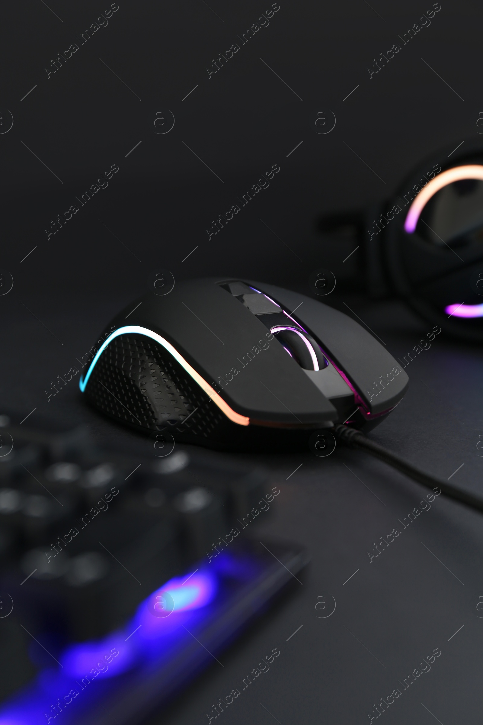 Photo of Computer mouse, RGB keyboard and headset on black background, selective focus