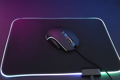 Photo of Computer mouse and mousepad in neon lights on dark background