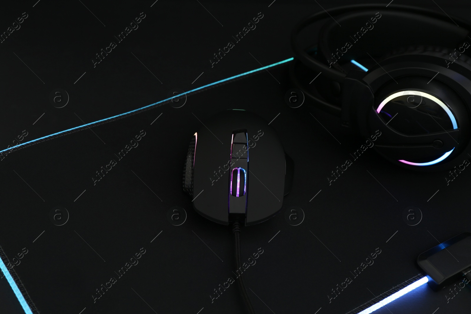 Photo of Computer mouse, mousepad and headset on black background, closeup