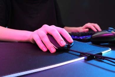 Gamer using modern wired computer mouse in neon lights at dark table, closeup