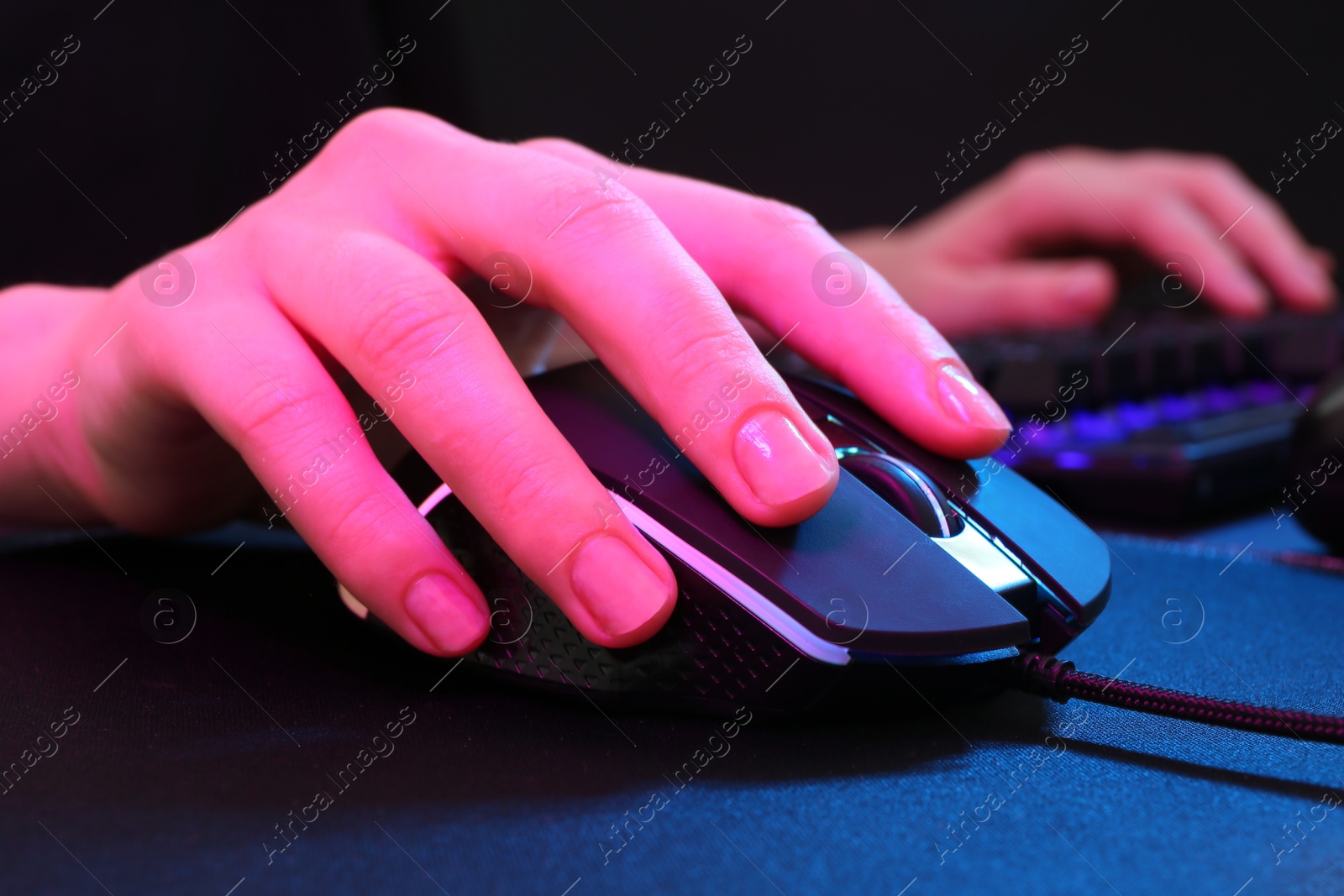 Photo of Gamer using modern wired computer mouse in neon lights at dark table, closeup