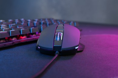 Photo of Computer mouse and RGB keyboard in neon lights on dark background, closeup